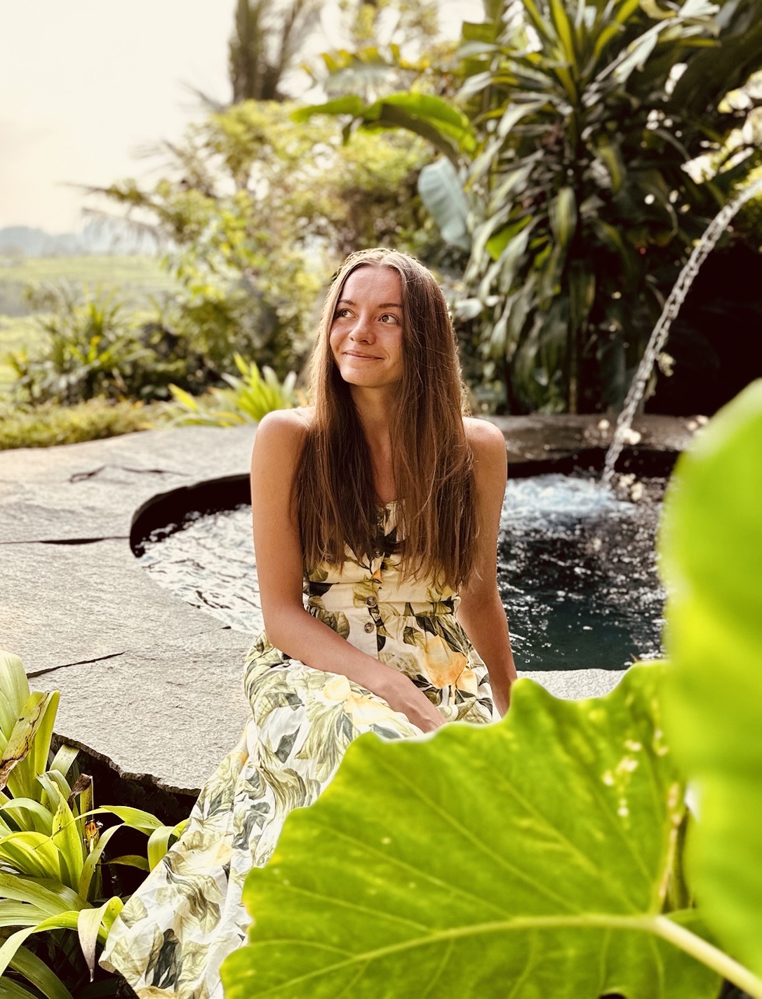 Yuliya sitting by a pool in a tropical garden, smiling