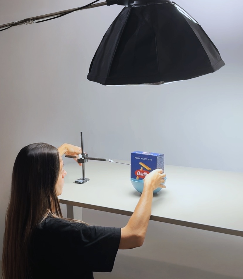 Behind the scenes: moving a box of Barilla penne above a blue bowl under a big studio light, with a rig holding it in place