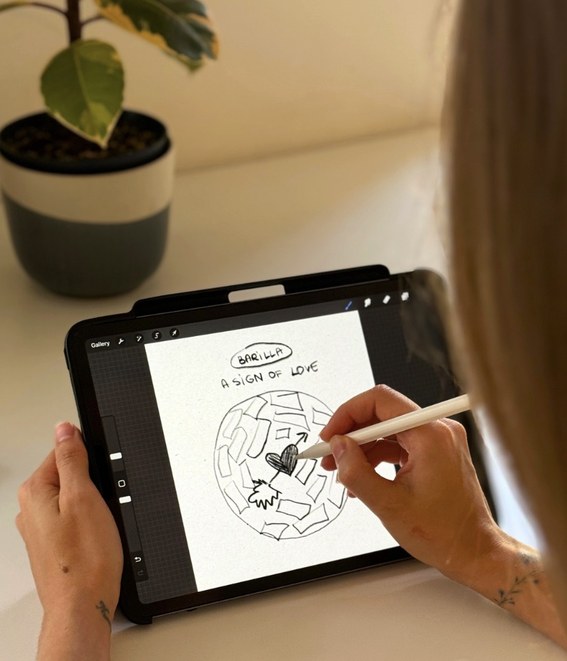 Sketching the storyboard on a tablet: a plate of pasta with a heart and an arrow, titled Barilla, A Sign of Love